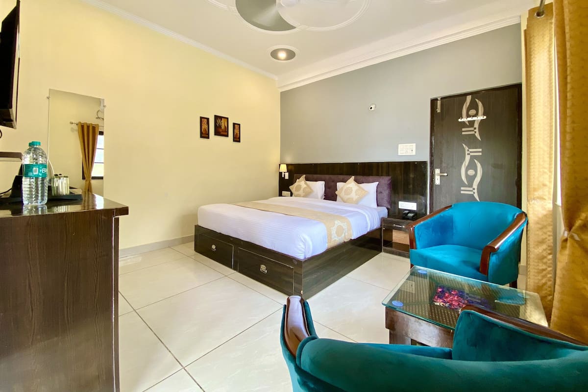 A hotel room with a bed, a desk with a water bottle, a blue chair, and a glass table.