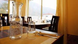 A clear glass bottle and a small glass on a table with a view of mountains through large windows. - Tapovan New Residency (5 minutes walk to Laxman jhula) (Narendranagar)