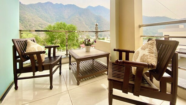 A balcony with two wooden chairs, a small table, and a potted plant. - Tapovan New Residency (5 minutes walk to Laxman jhula) (Narendranagar)