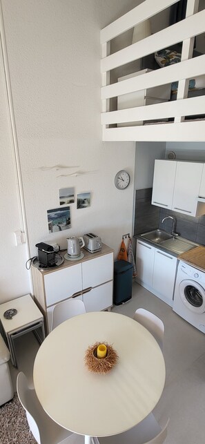Une petite cuisine équipée comprenant un évier, un lave-linge et un coin repas avec une table et des chaises.