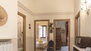 A hallway with a radiator, a bed with a white bedspread, a chair, a wooden wardrobe, and a television on a stand. - Villa a Montaione ID 3114 (Montaione)