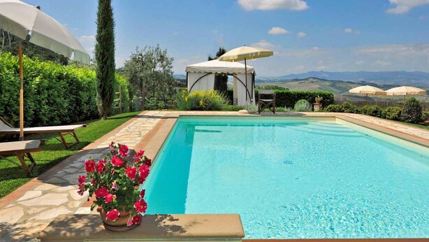 A rectangular swimming pool with a clear blue water surface, surrounded by a stone deck. There are white umbrellas and a gazebo-like structure with a white canopy. - Villa a Montaione ID 3114 (Montaione)