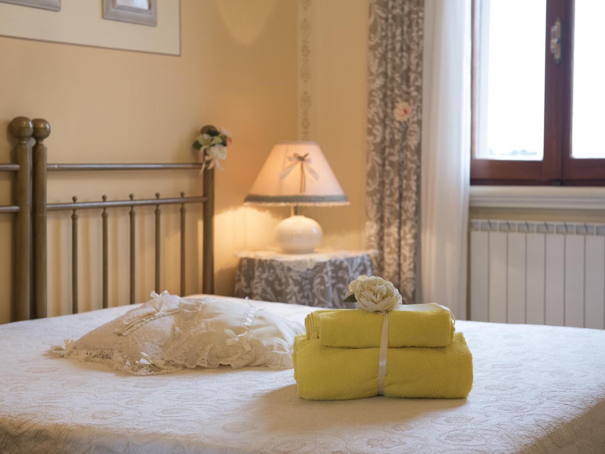 A neatly made bed with a white lace pillow and a yellow towel bundle.