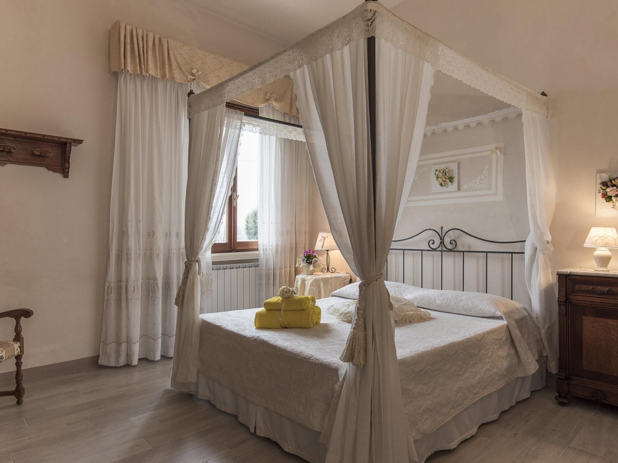 Une chambre à coucher avec un lit à baldaquin, une table de chevet en bois, une petite table de chevet avec une lampe et une fenêtre ornée de rideaux légers.