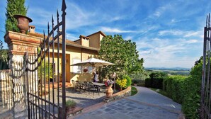 A gated entrance with a stone wall, a patio with outdoor furniture, and a view of the countryside. - Villa a Montaione ID 3114 (Montaione)