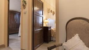 A hallway with a wooden door, a bedside table with a lamp, and a chair with a pillow. - Villa a Montaione ID 3114 (Montaione)