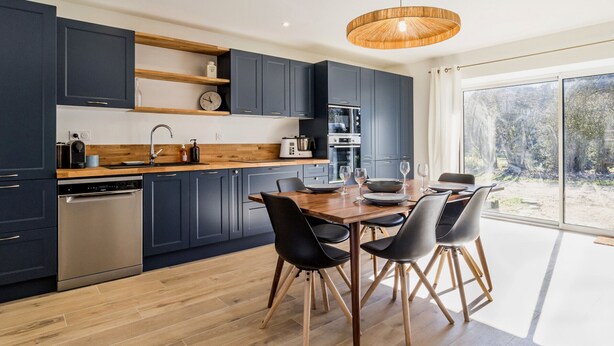 A modern kitchen with dark cabinets, wooden countertops, and a dining area with a large table and chairs. - Charming Cottage near Loire: Private Terrace, 2 Ensuite BRs, Baby Gear, WiFi, Pet-Friendly (Mauves-sur-Loire)