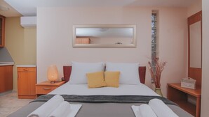 Ein Hotelzimmer mit einem Bett, einem Nachttisch mit Lampe, einem Spiegel, einer kleinen Kommode und einer Vase mit Trockenpflanzen.