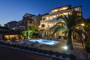A two-story building with a swimming pool, outdoor seating, and palm trees.