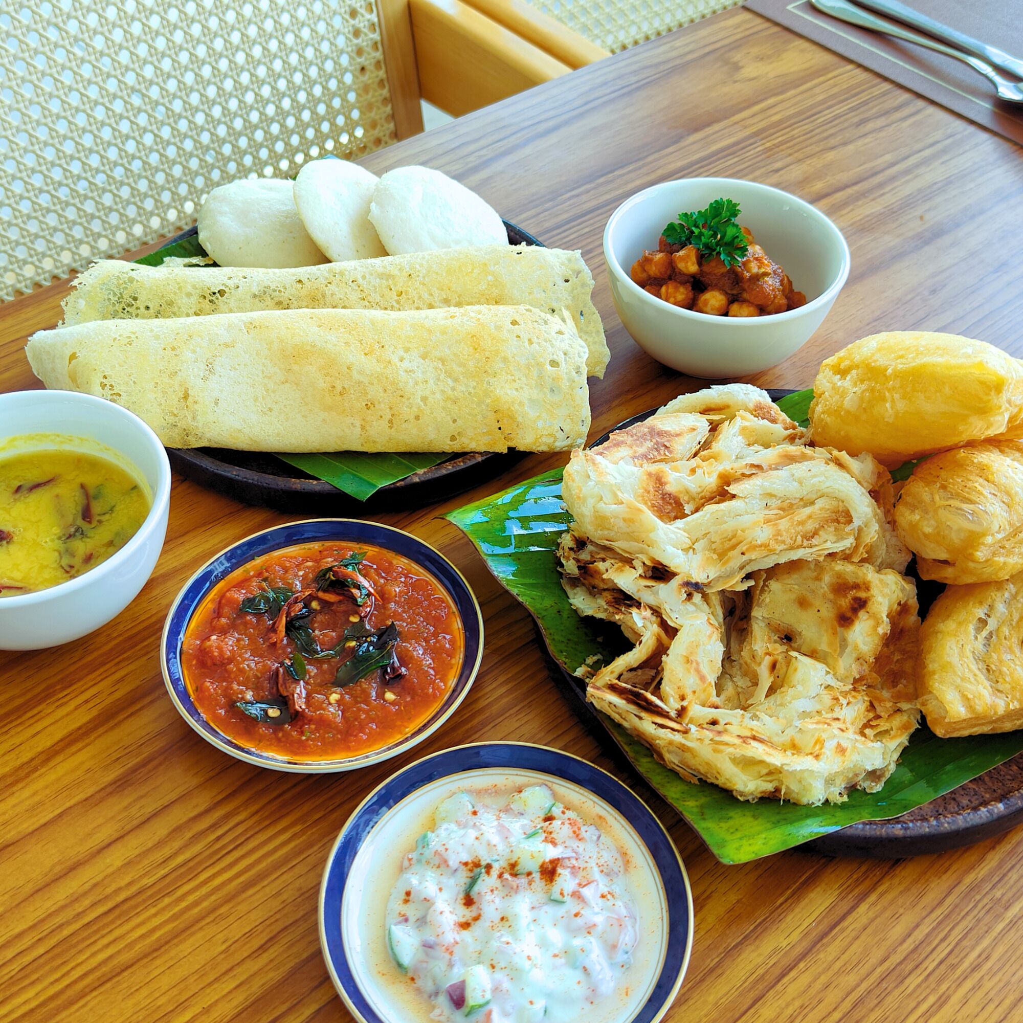 A table with food items including a plate of idlis, a bowl of chutney, and a bowl of soup.