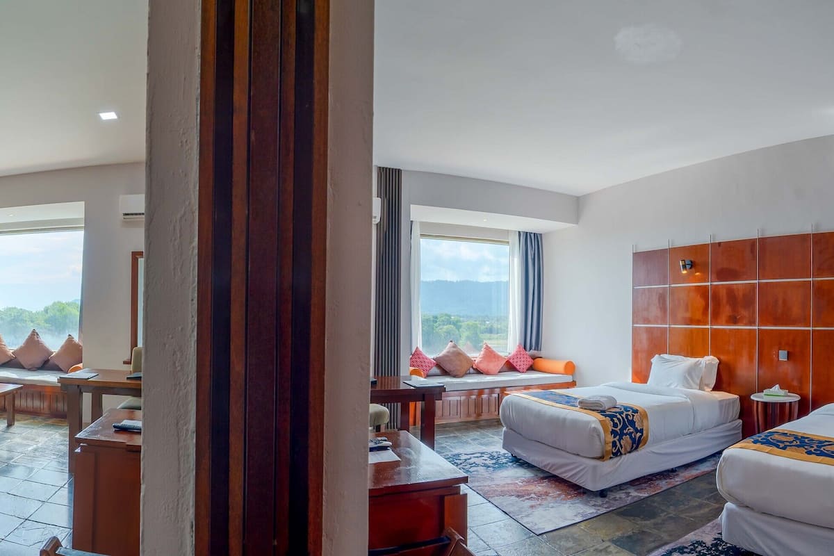 Una habitación de hotel con una cama, una zona de estar con una mesa y sillas, un ventanal con vistas y un cabecero de madera.