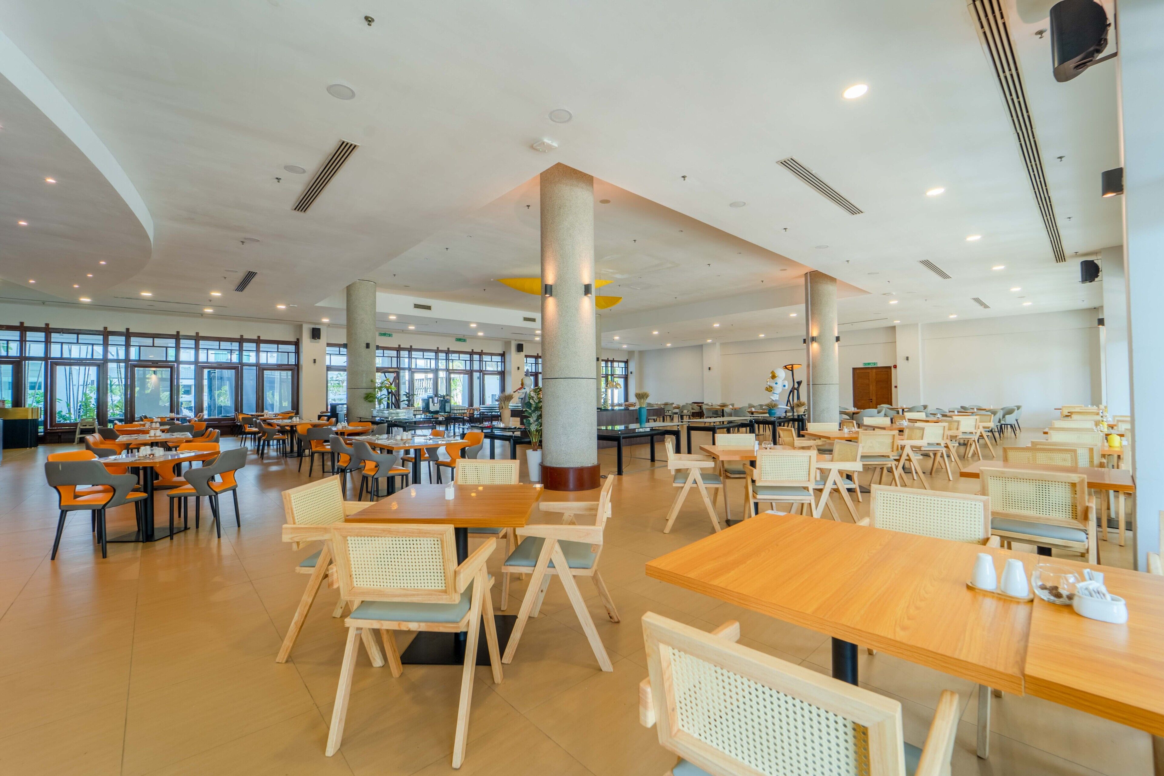 Una amplia cafetería con varias mesas y sillas, ventanas grandes y un techo alto con iluminación empotrada.