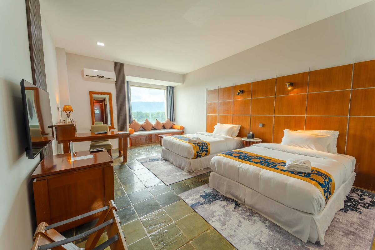 Habitación de hotel con dos camas, un escritorio, una silla, un televisor y vistas a las montañas.