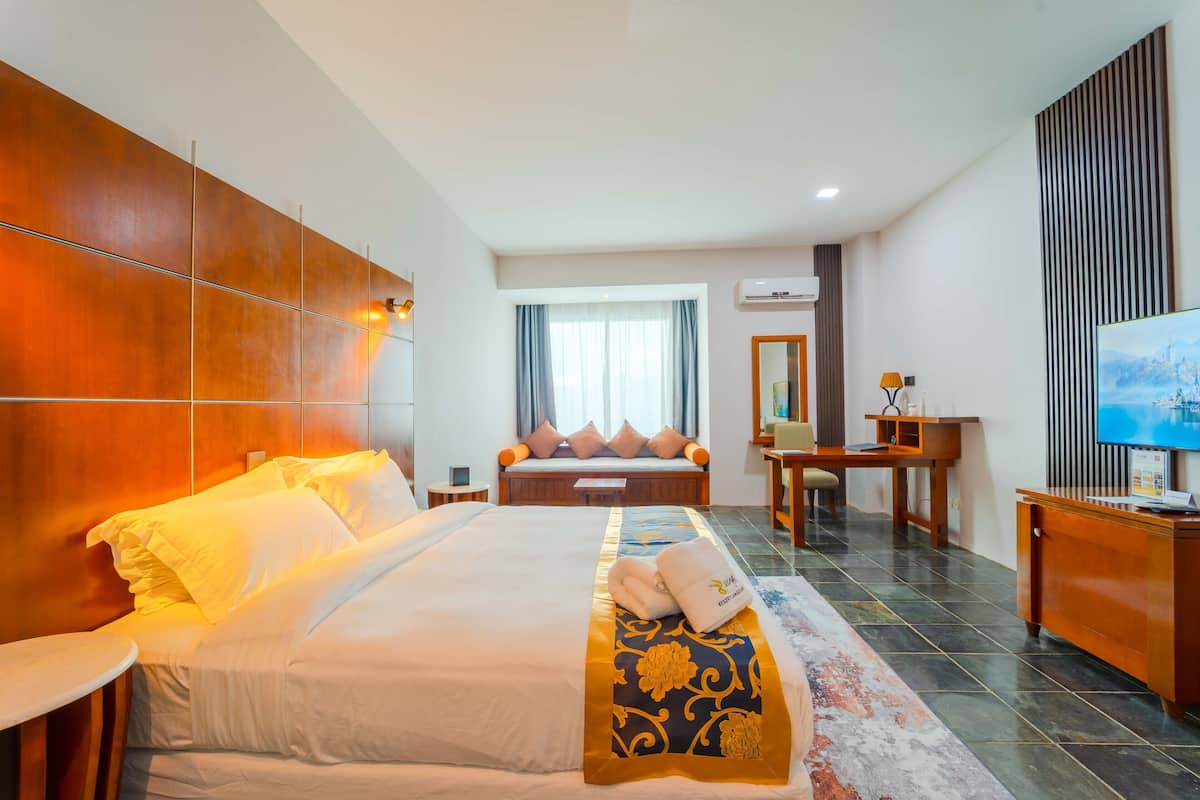 Habitación de hotel con una cama grande, un escritorio, una silla, un televisor y una ventana con cortinas.