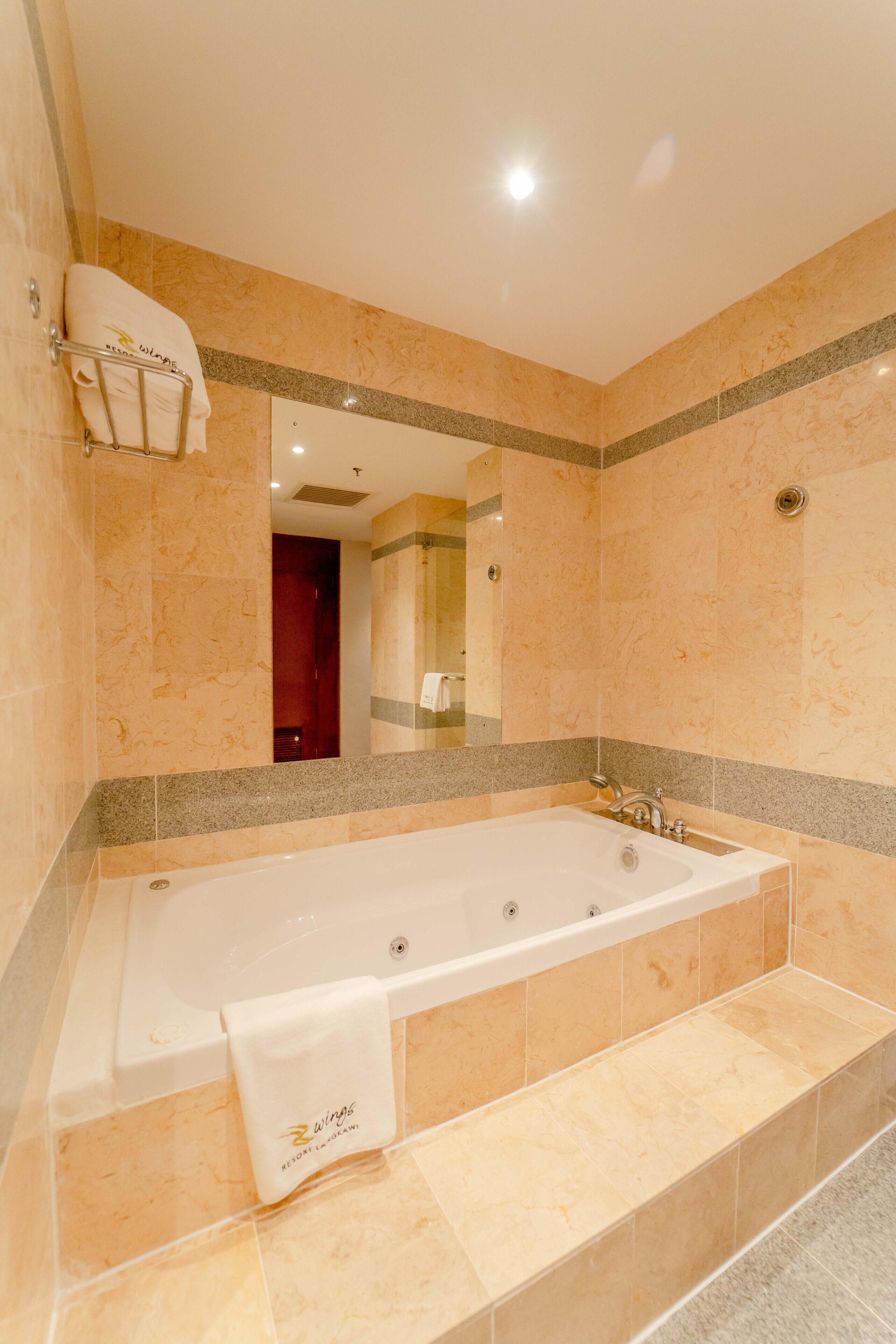 Una bañera grande y rectangular con una toalla colgando al lado, un espejo encima y un perchero en la pared.