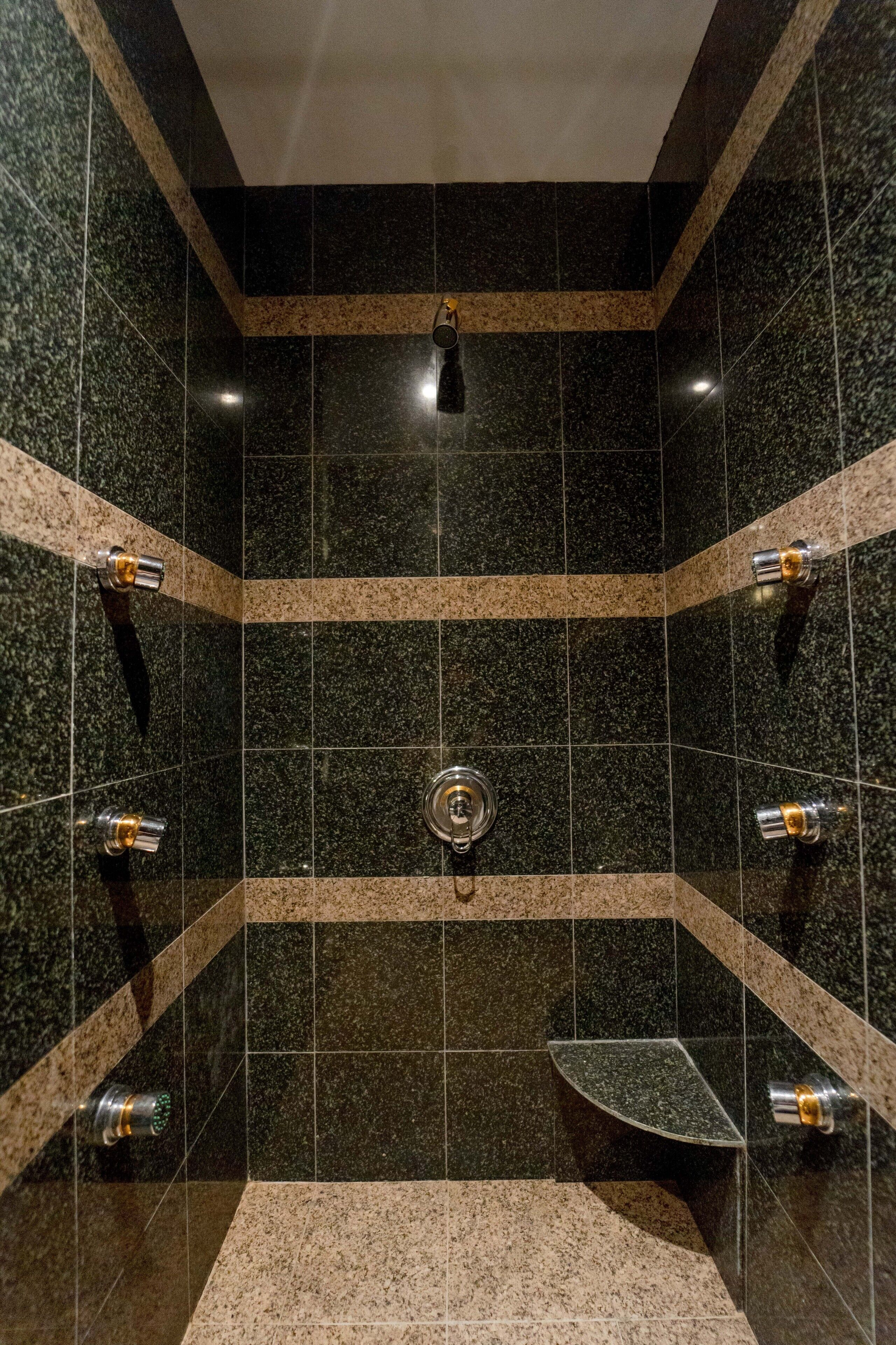 A modern bathroom with dark granite tiles, a central sink, and a curved bathtub.