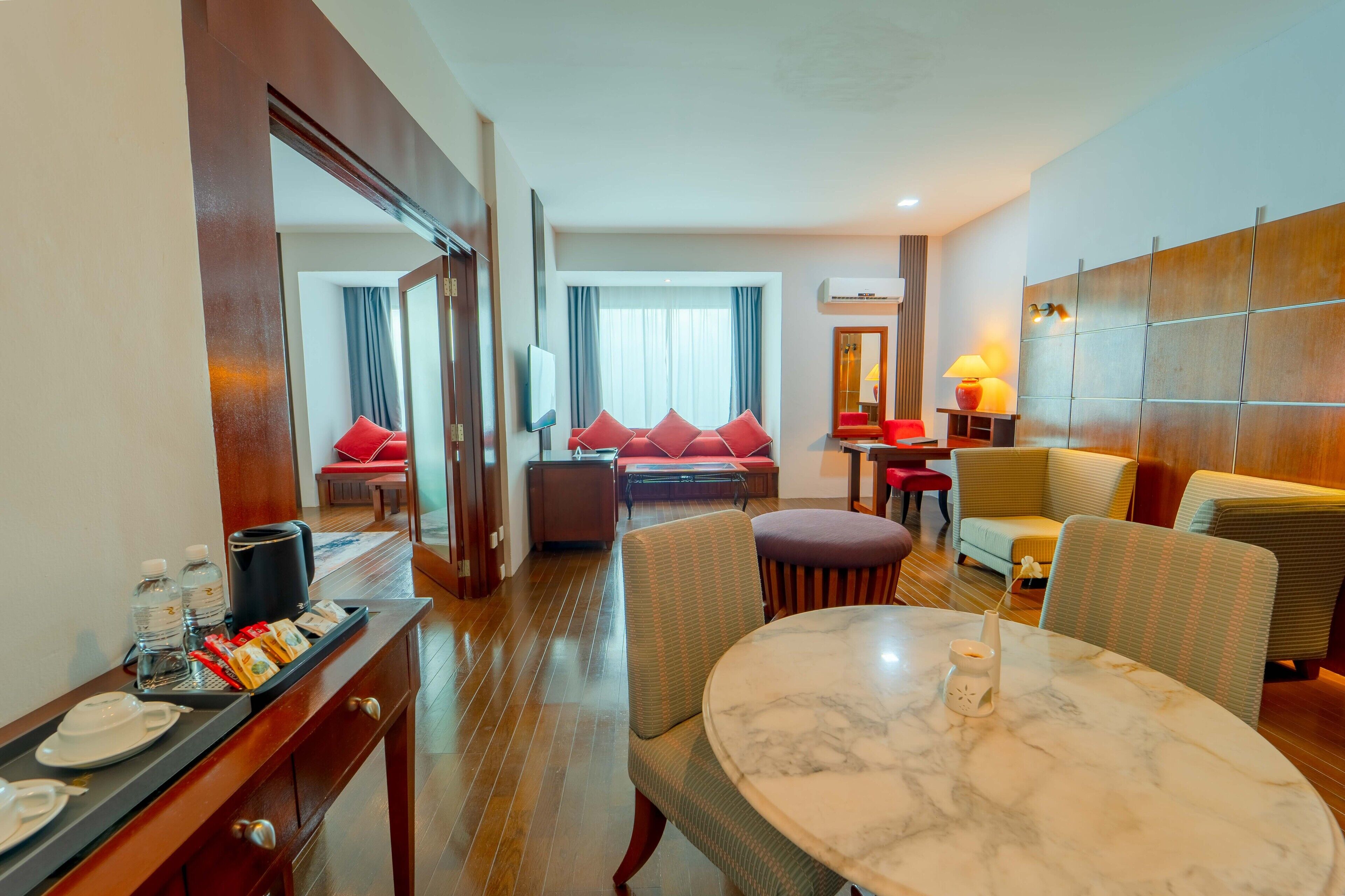 A hotel room with a dining area, a sofa set, a TV, and a minibar.