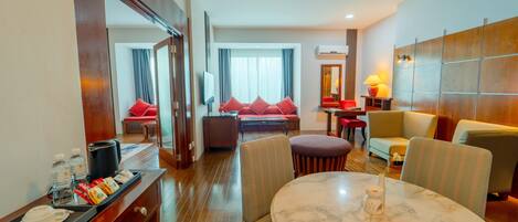 A hotel room with a dining area, a sofa set, a TV, and a minibar.