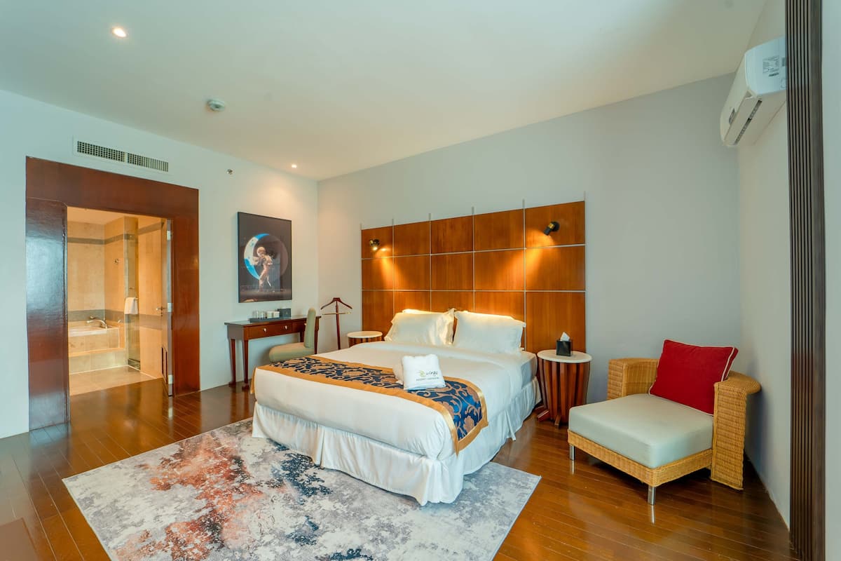 Una habitación de hotel moderna con una cama grande, un pequeño sofá, un baño con cabina de ducha de cristal y un cabecero de madera.