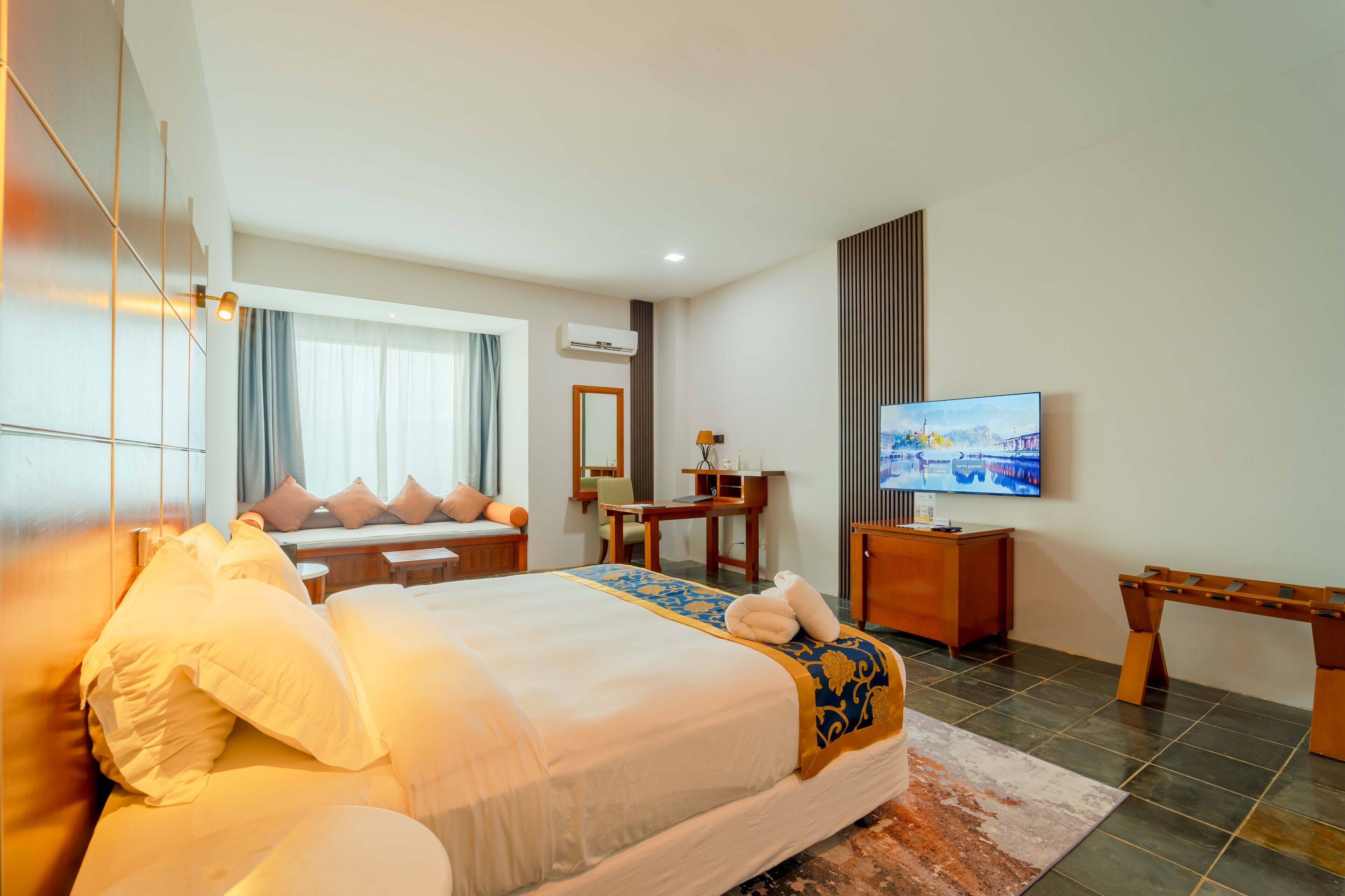 Een hotelkamer met een groot bed, een bureau, een televisie en een raam met gordijnen.