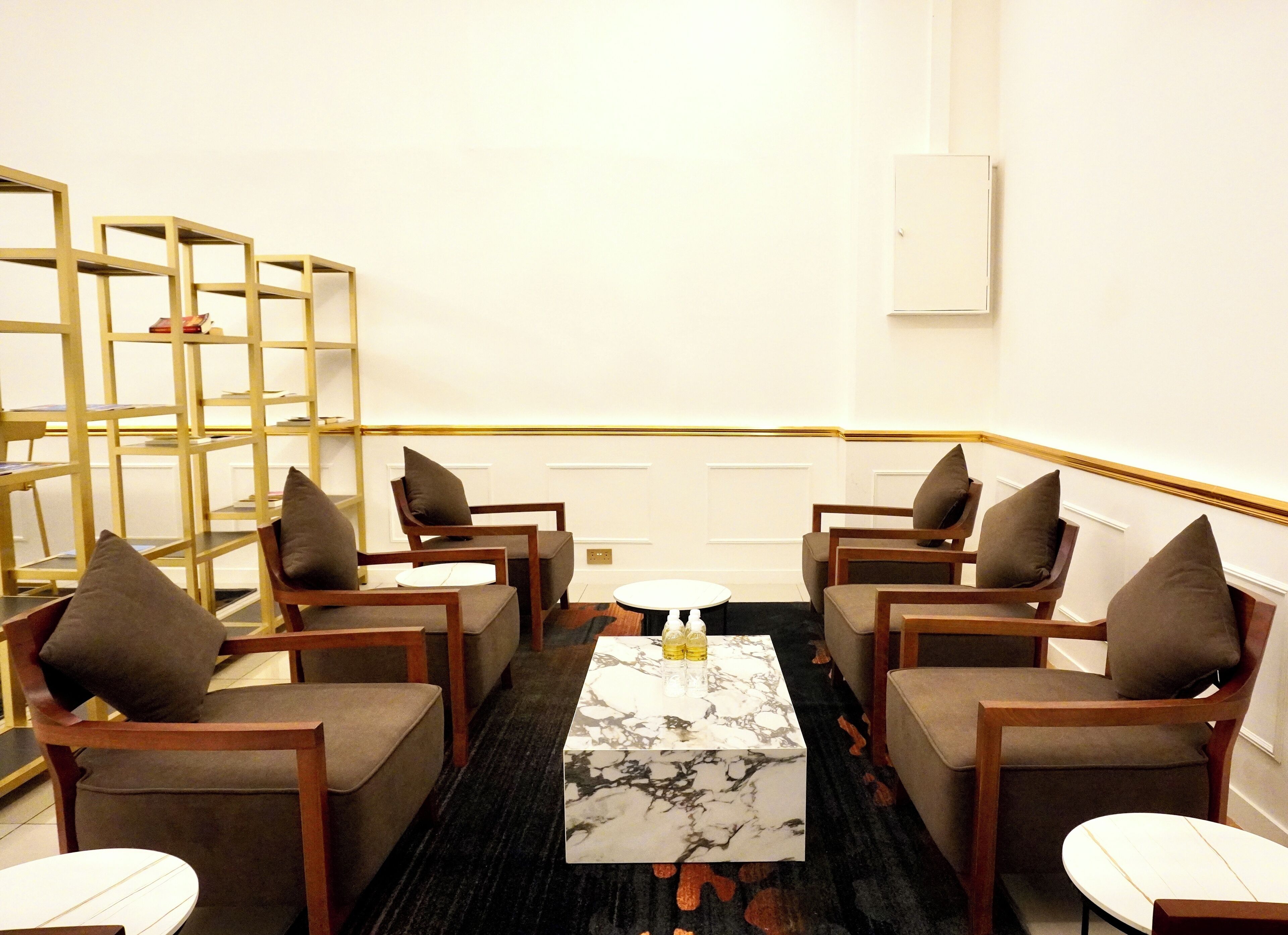 Ein moderner Lounge-Bereich mit einem Marmortisch, bequemen Sitzgelegenheiten und einem goldgerahmten Bücherregal.