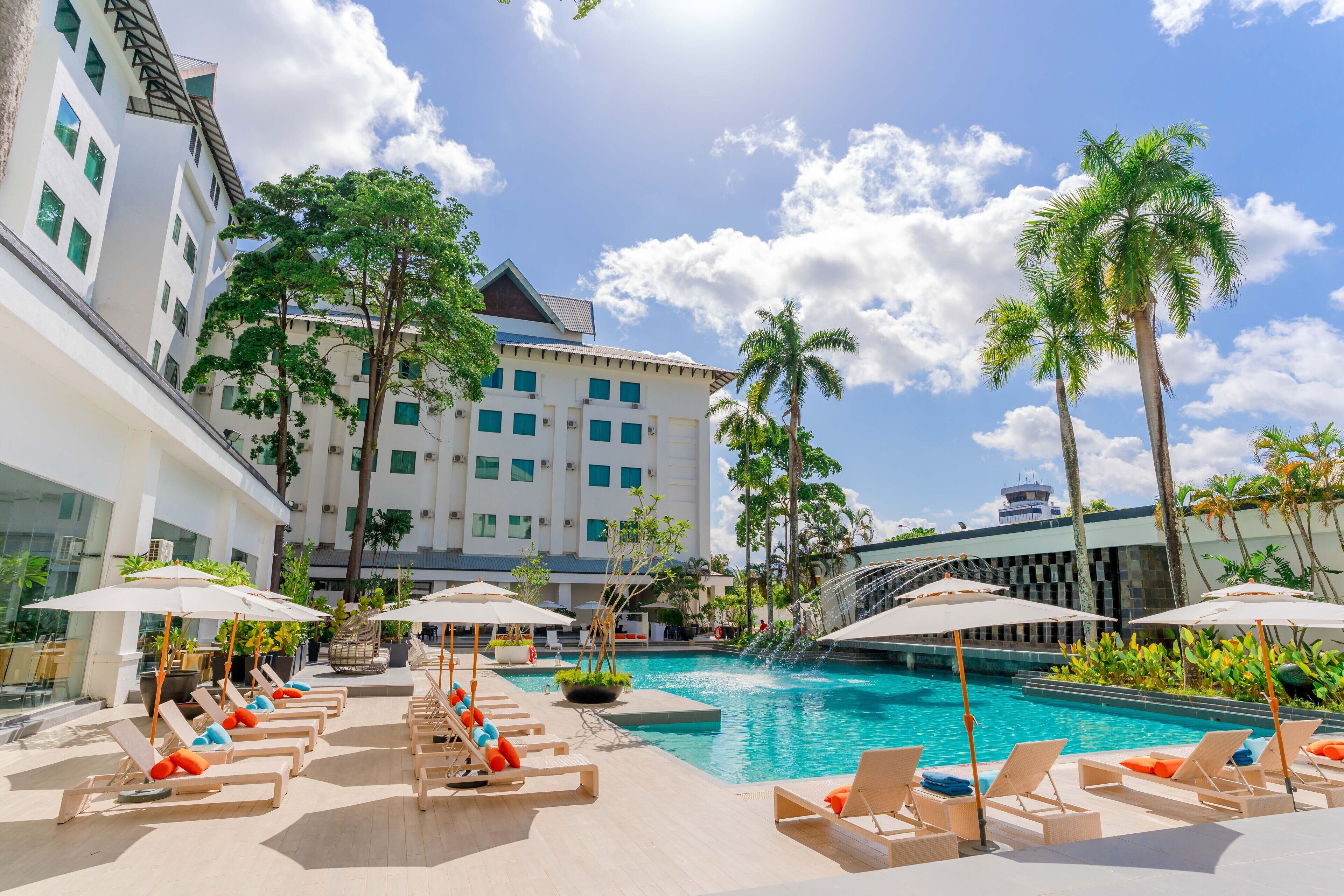 Área de piscina de hotel com espreguiçadeiras, guarda-sóis e palmeiras.