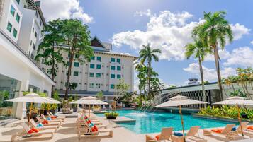 Área de piscina de hotel com espreguiçadeiras, guarda-sóis e palmeiras.