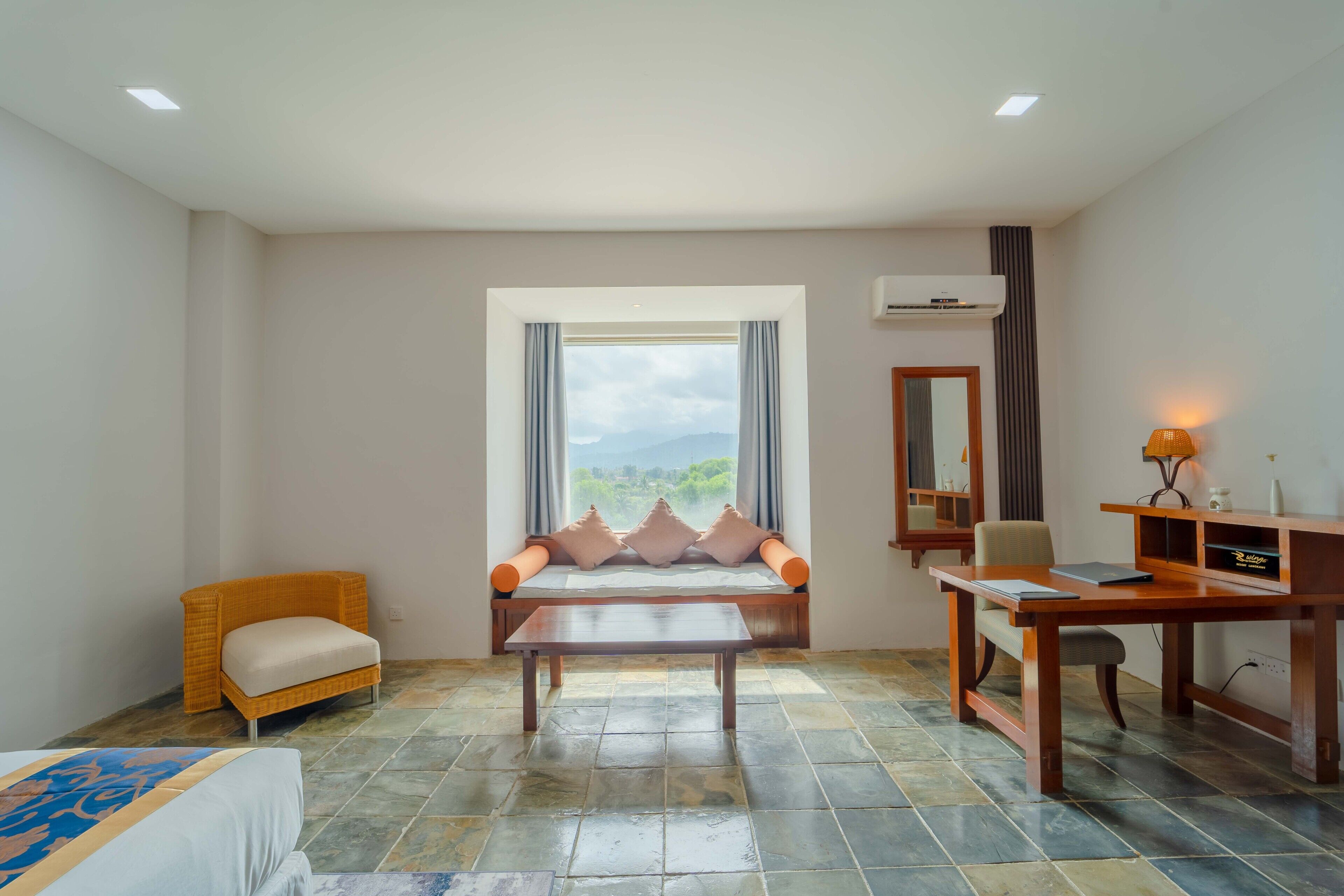 Habitación de hotel con cama, sofá, mesa y escritorio. Se aprecia una ventana con vistas al exterior.