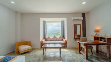 Habitación de hotel con cama, sofá, mesa y escritorio. Se aprecia una ventana con vistas al exterior.