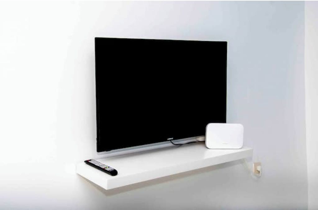 Un téléviseur à écran plat, posé sur un meuble blanc, avec une télécommande à côté.