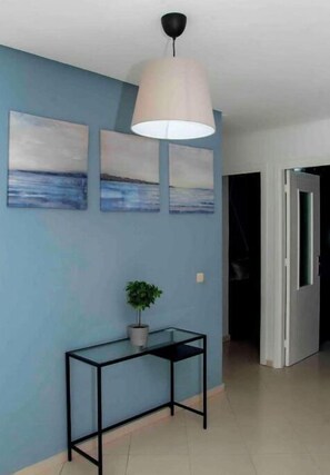 Un couloir avec un mur bleu, une console noire sur laquelle est posée une plante, et un luminaire suspendu blanc.