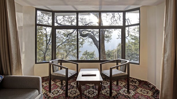A room with a bay window, two chairs, a small table, and a patterned carpet. - Treebo Kosmos Anamika, 1 Km From Nainital Lake (Nainital)