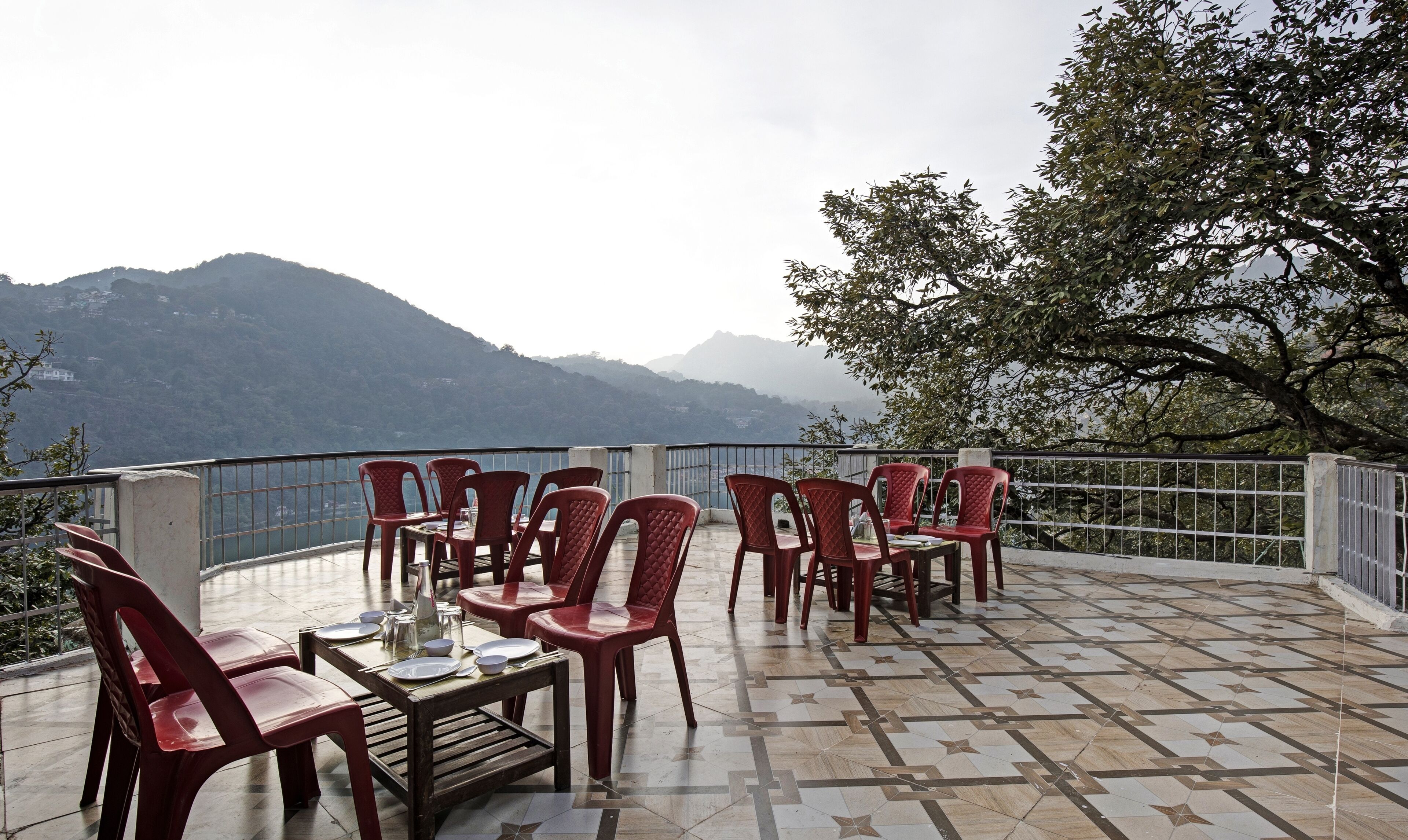 A terrace with red plastic chairs and a table, overlooking a mountainous landscape.