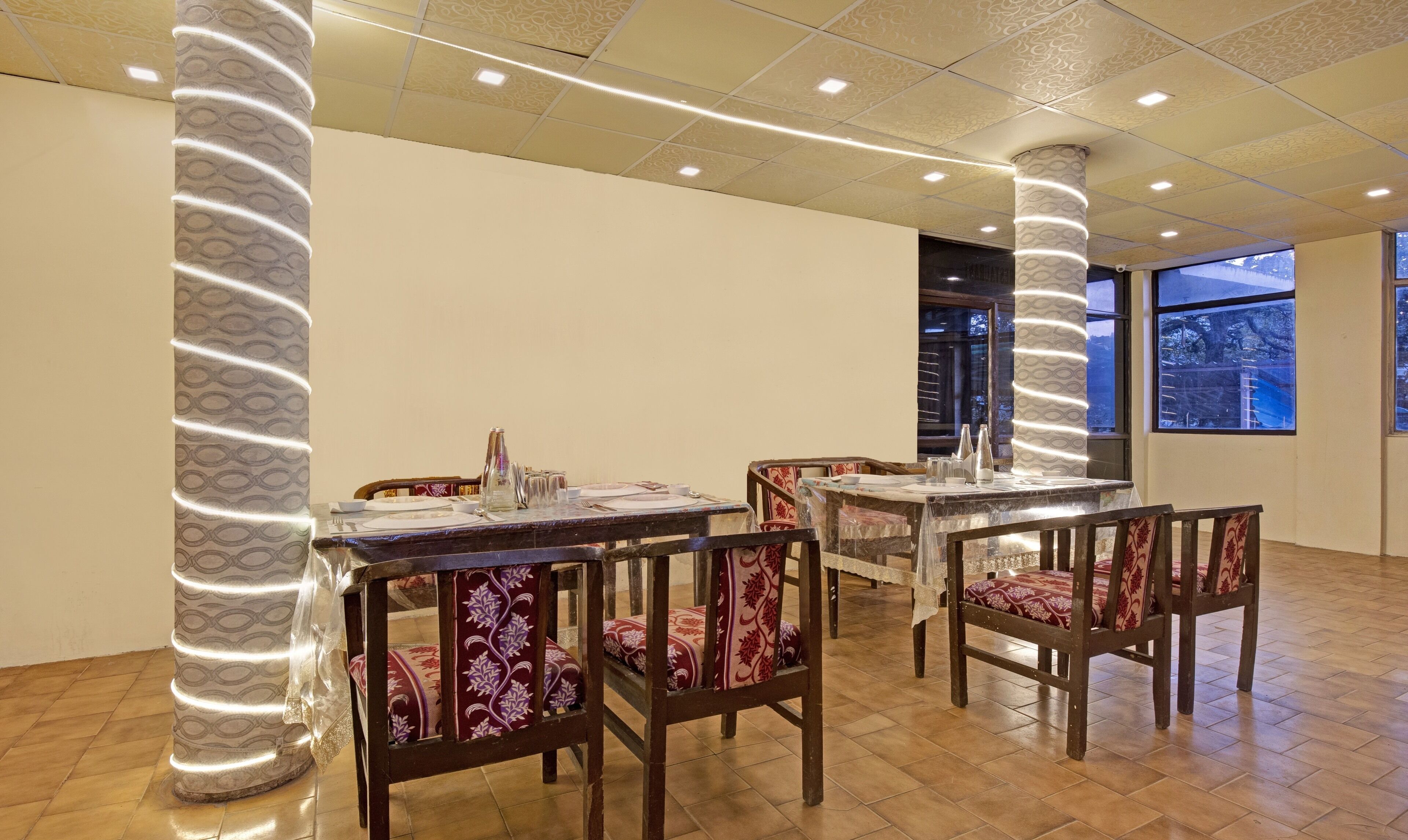 Un espace repas avec des tables et des chaises en bois, une colonne décorée et une vue par la fenêtre.