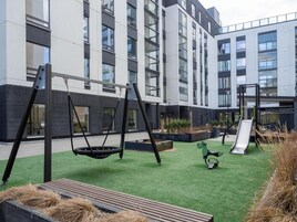 A playground with swings and a slide, surrounded by a building with large windows and a flat roof.