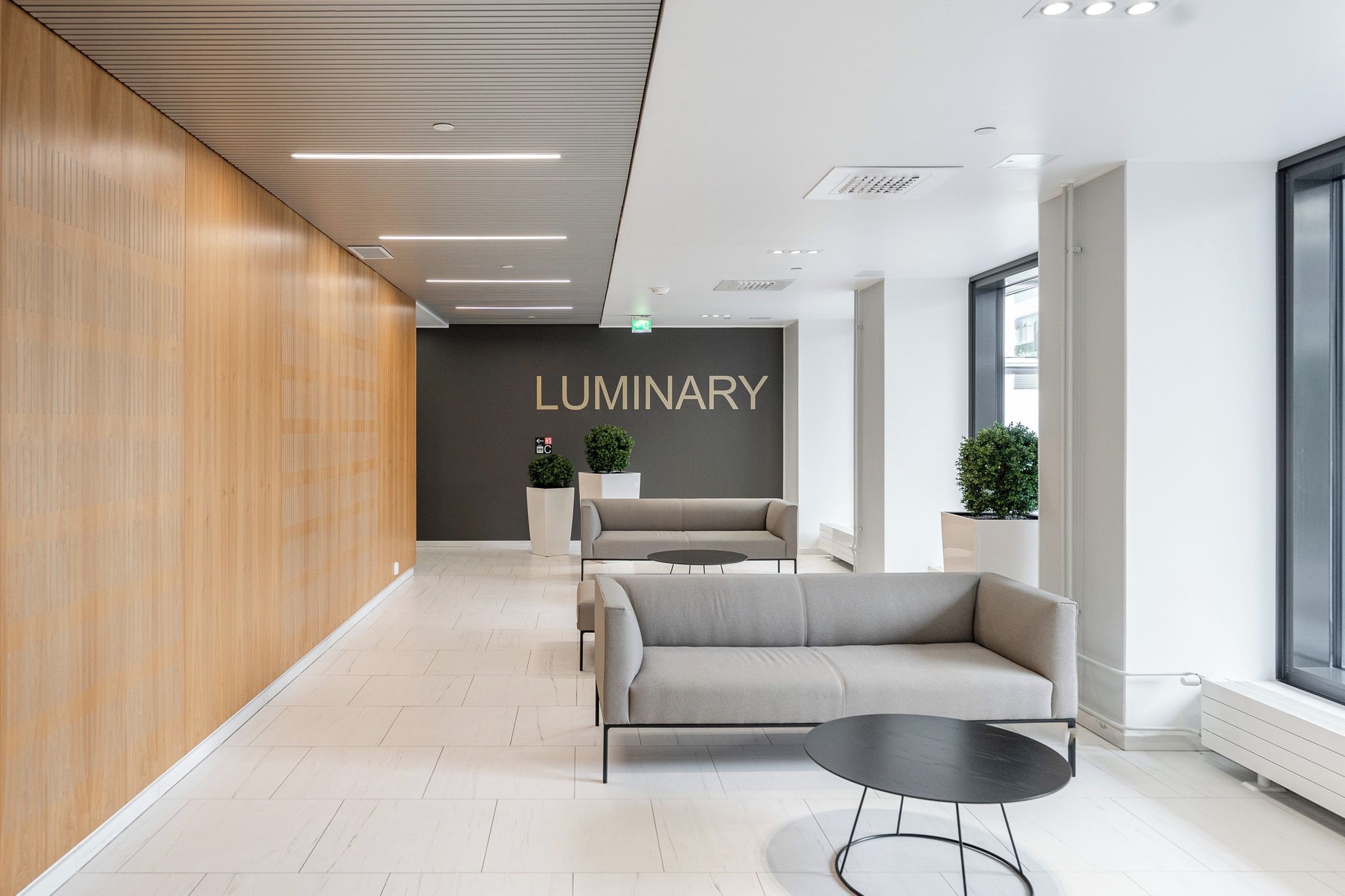 Un vestíbulo moderno con mostrador de recepción, área de descanso y una pared con la señalización 'LUMINARY'.