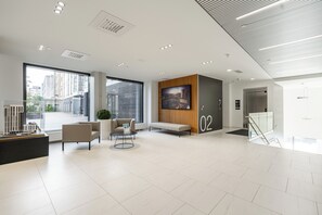 Un hall d’entrée moderne doté d’un comptoir de réception, d’un espace salon et de grandes fenêtres offrant une vue sur le paysage urbain.