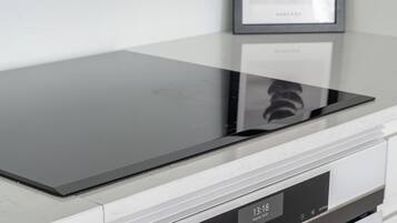 Una cocina con una placa de cocción por inducción negra, un horno de acero inoxidable y un cuadro de un aguacate en la pared.