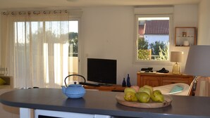 Una sala de estar con televisor, hervidor, frutero y ventana con vista a árboles.