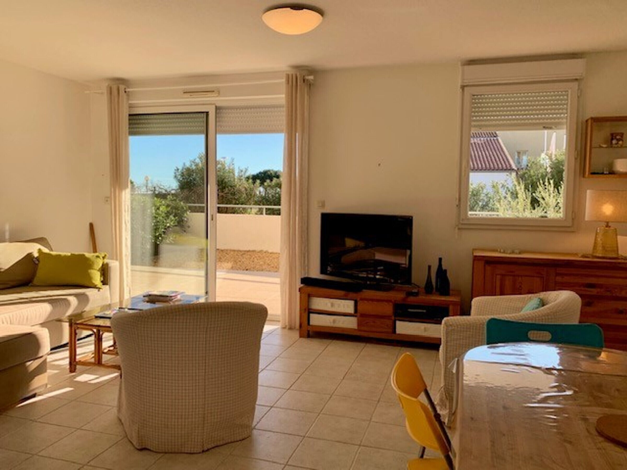 Een woonkamer met een bank, een stoel, een televisie en een tafel. Er is een glazen schuifdeur die uitkomt op een balkon.