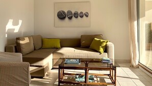 Una sala de estar con un sofá color beige, una mesa de centro de vidrio y una obra de arte colgada en la pared.