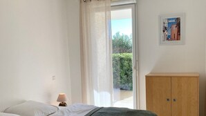 Un dormitorio con cama, mesita de noche, lámpara, armario de madera y vista a la vegetación.