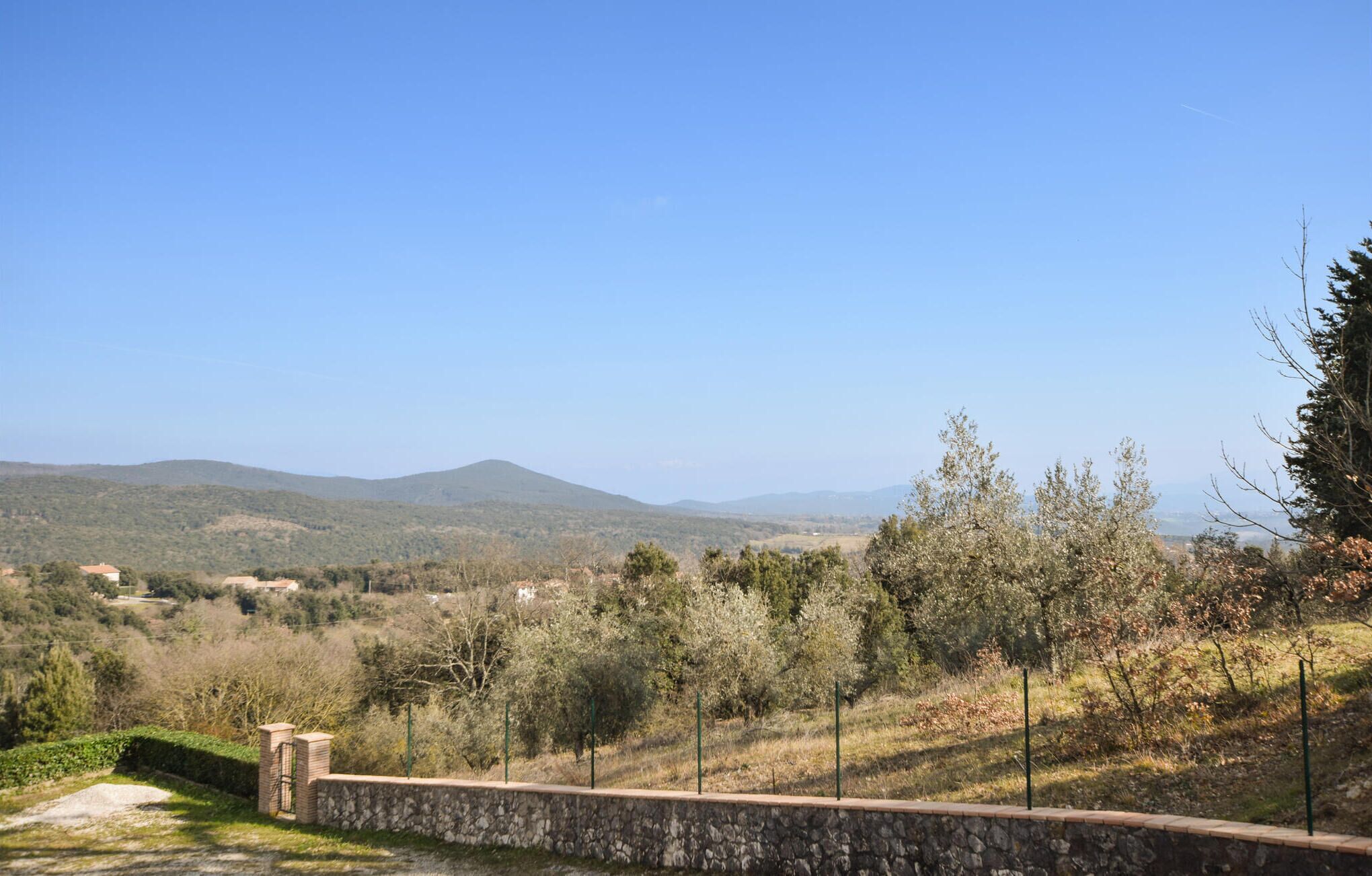 Un muro de piedra con una verja, con vistas a un paisaje rural con árboles y colinas lejanas.