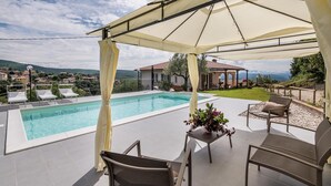 A poolside area with a covered seating area, a pool, and a view of a residential area with houses and mountains in the background. - Lovely home in Amelia with kitchen (Amelia)