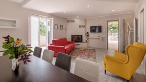 A spacious living room with a red sofa, a yellow armchair, and a dining table with chairs. A flat-screen TV is mounted on the wall, and there is a large window providing natural light. - Lovely home in Amelia with kitchen (Amelia)