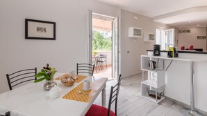 A modern kitchen with white cabinets, a coffee maker, and a kettle. There is a dining area with a table set for two, a vase with flowers, and a framed picture on the wall. - Lovely home in Amelia with kitchen (Amelia)