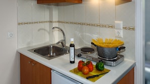 A kitchen with a sink, stove, and a cutting board with tomatoes and a green pepper. - Room25 (Chania)