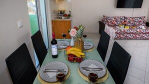 A dining area with a table set for four, including plates, cutlery, and glasses, with a fruit bowl and a bottle of wine. - Room25 (Chania)