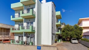A multi-story building with balconies, a car parked in front, and a clear blue sky. - Room25 (Chania)