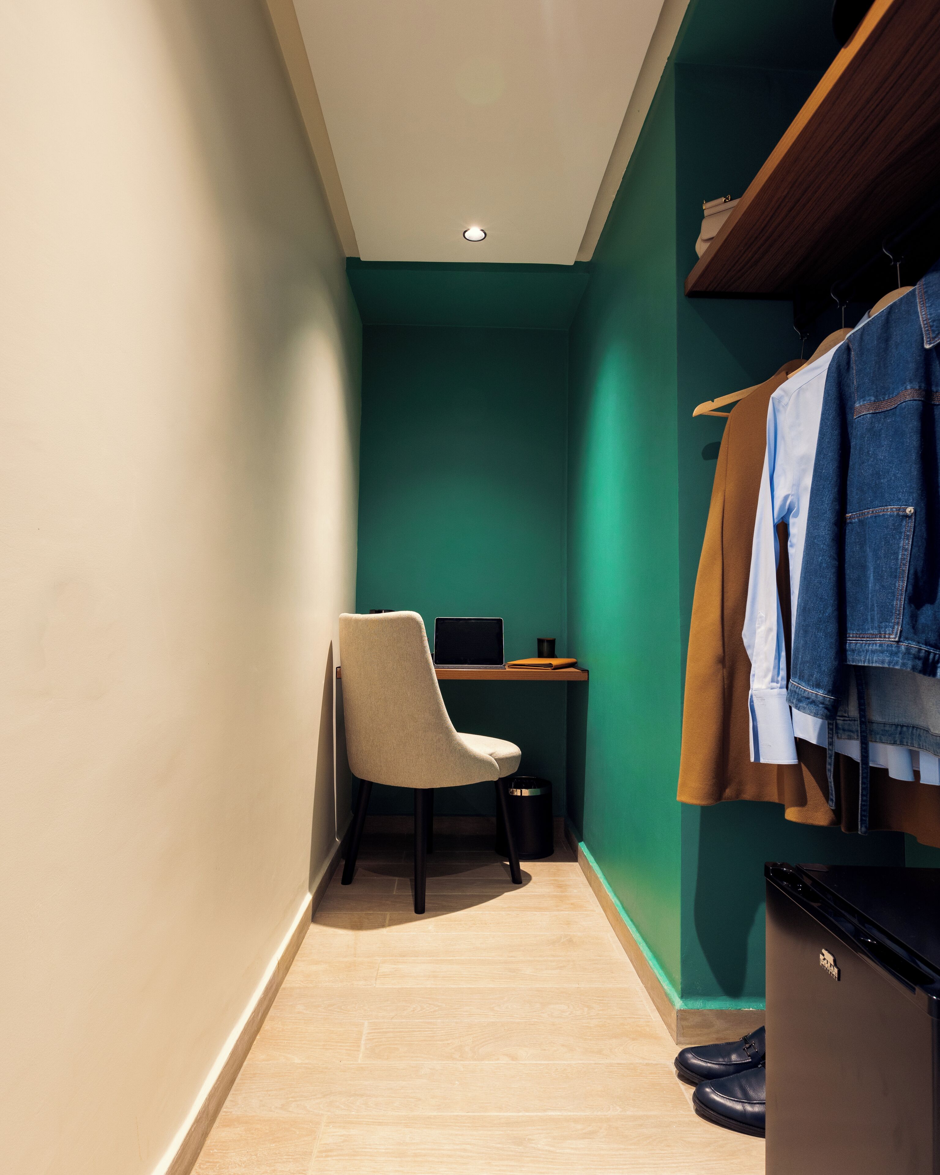 A narrow hallway with a desk, chair, and a clothing rack with jackets.